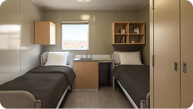 Modern shared dorm-style room with two single beds, neutral decor, and compact furnishings operated by remote site catering companies.