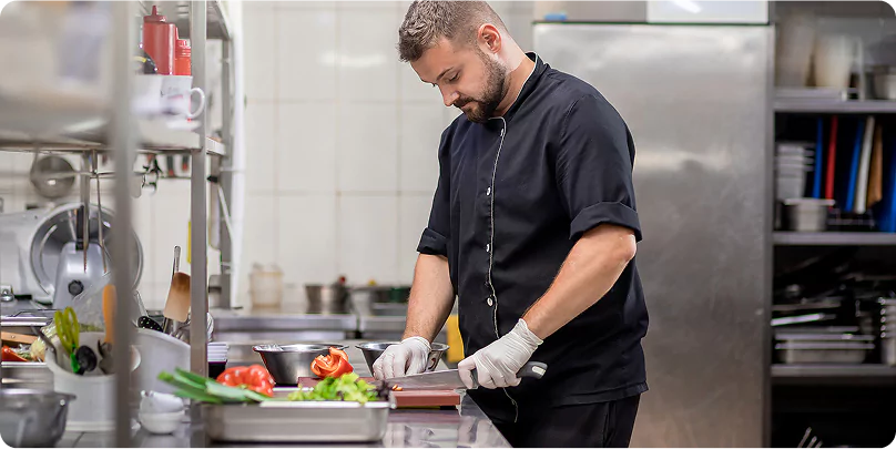 Private Workforce Camp Room At Remote Site Chef in black uniform preparing fresh vegetables in a remote camp kitchen.