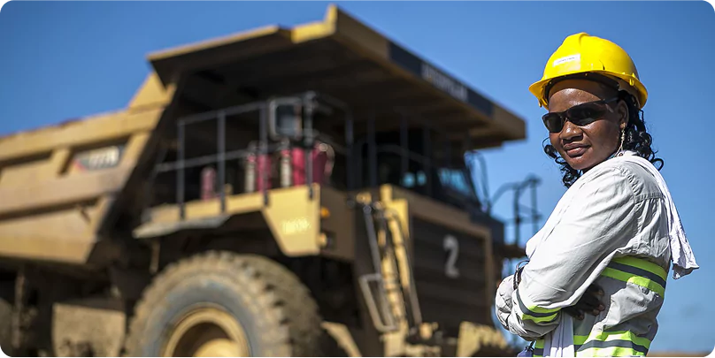 FIFO Worker at Remote Job Site Female FIFO mine worker wearing safety gear standing in front of a large haul truck at a remote site.