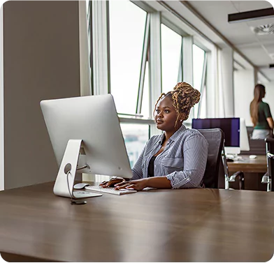 Travel Coordinator Working at Desk in Modern Office Travel coordinator at desk working on a desktop computer in a bright, modern office setting.