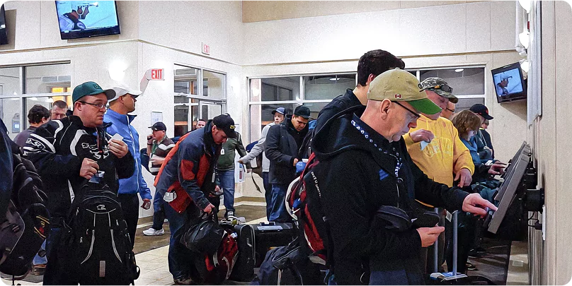 FIFO workers with luggage checking in at self-service kiosks inside a remote camp facility.