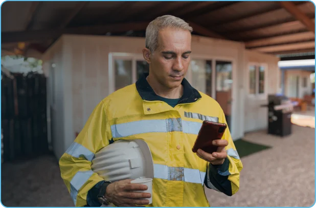 Fifo workers holds coffee and reads phone outside of camp bedroom constructed of prefabricated materials.