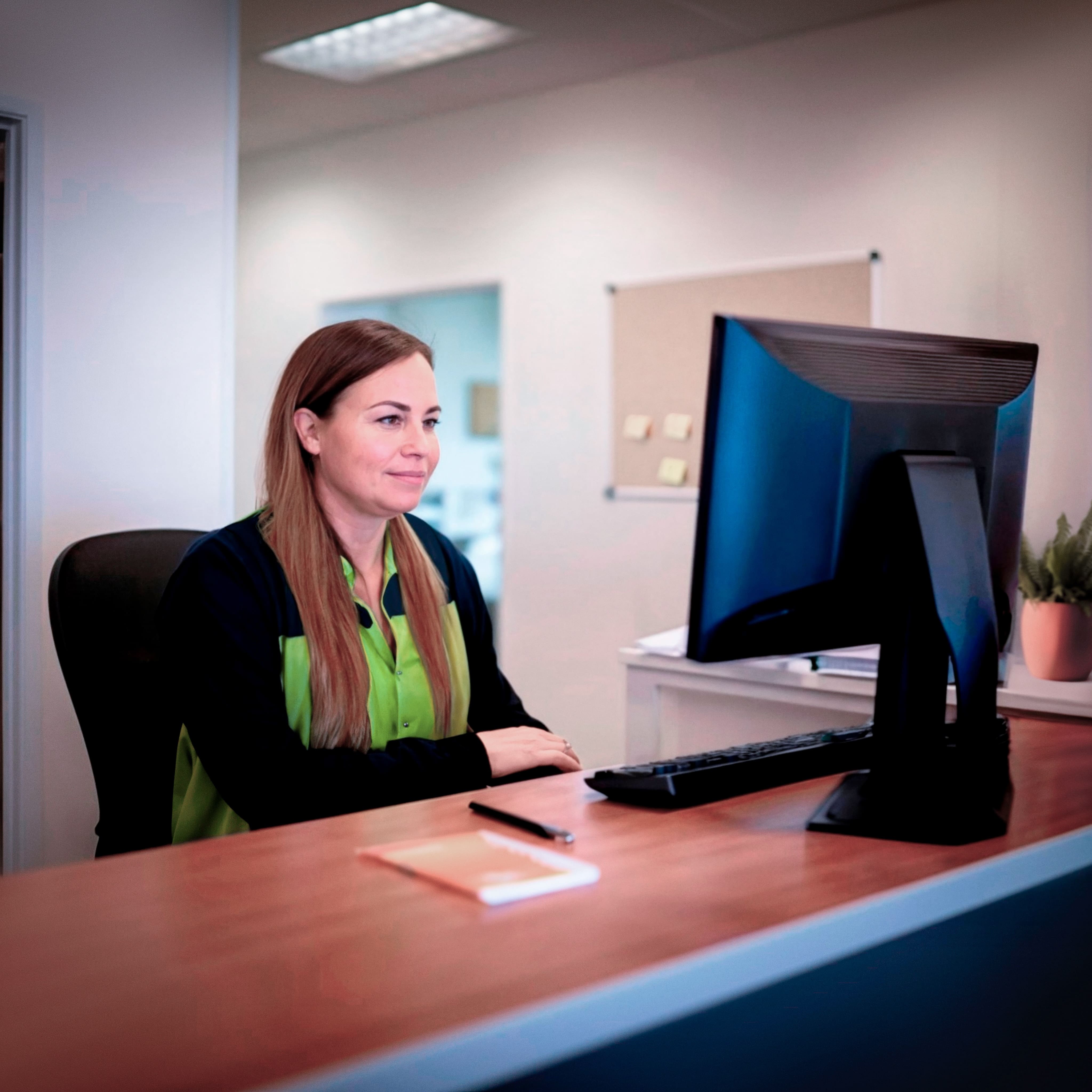 Woman in uniform sits at reception desk staring at a computer monitor.
