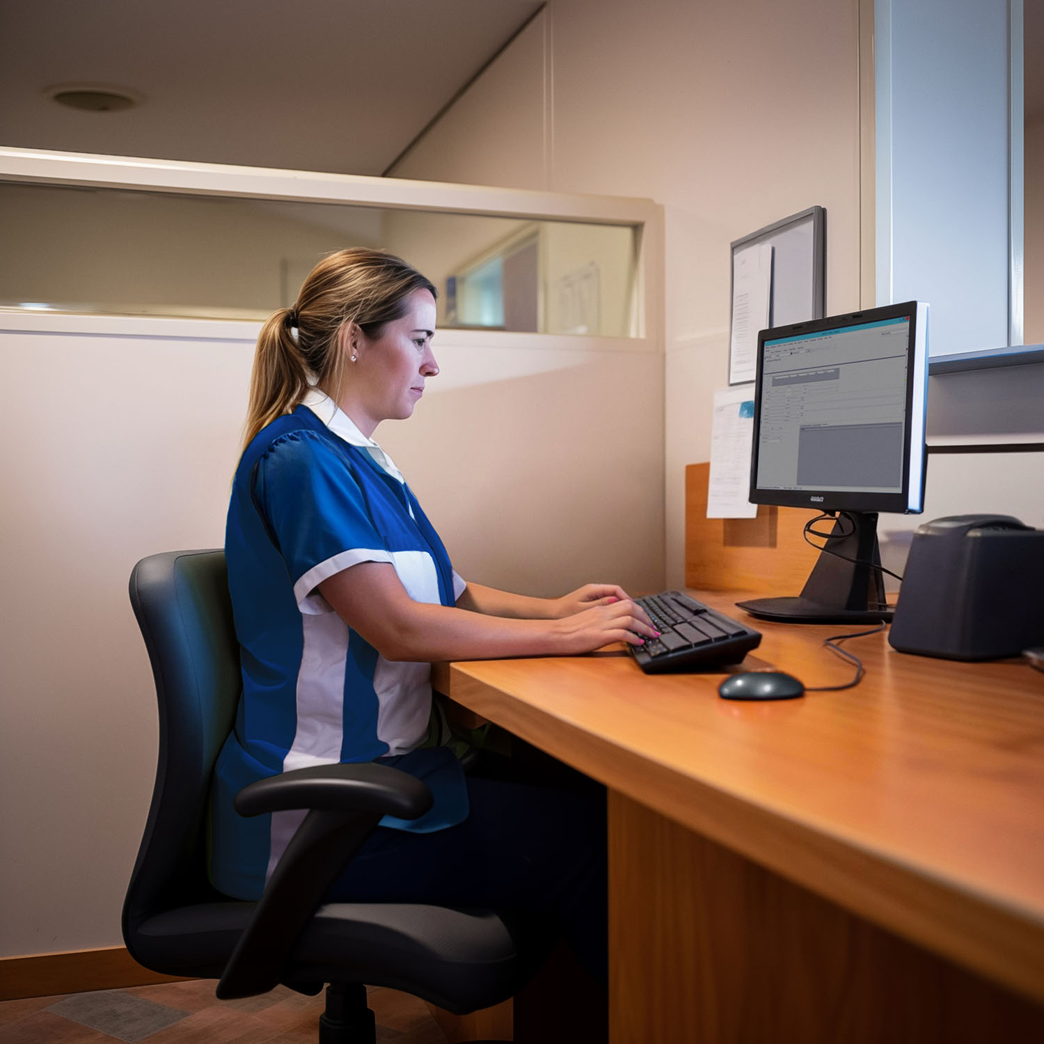 Woman in uniform types at desk in a small office setting.
