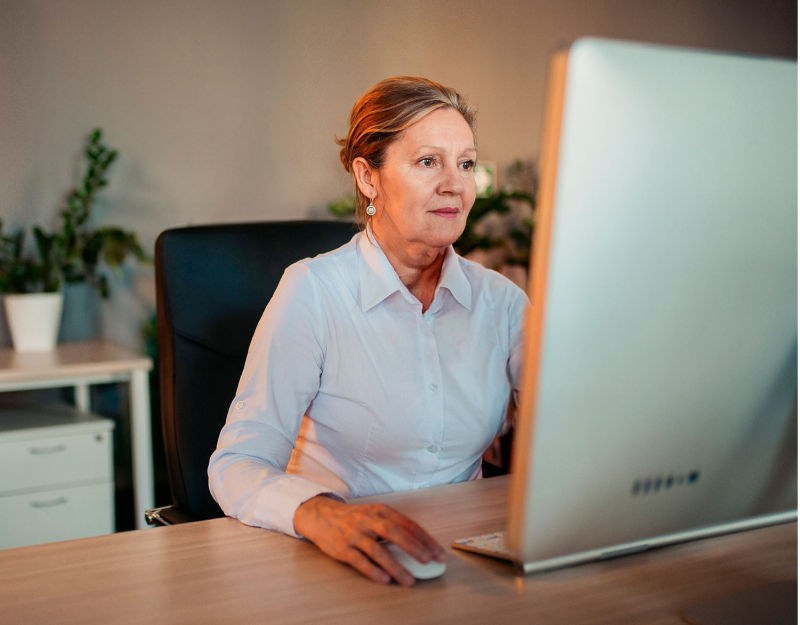 Woman wearing a white collared shirt clicks on something as she stares at a computer monitor.