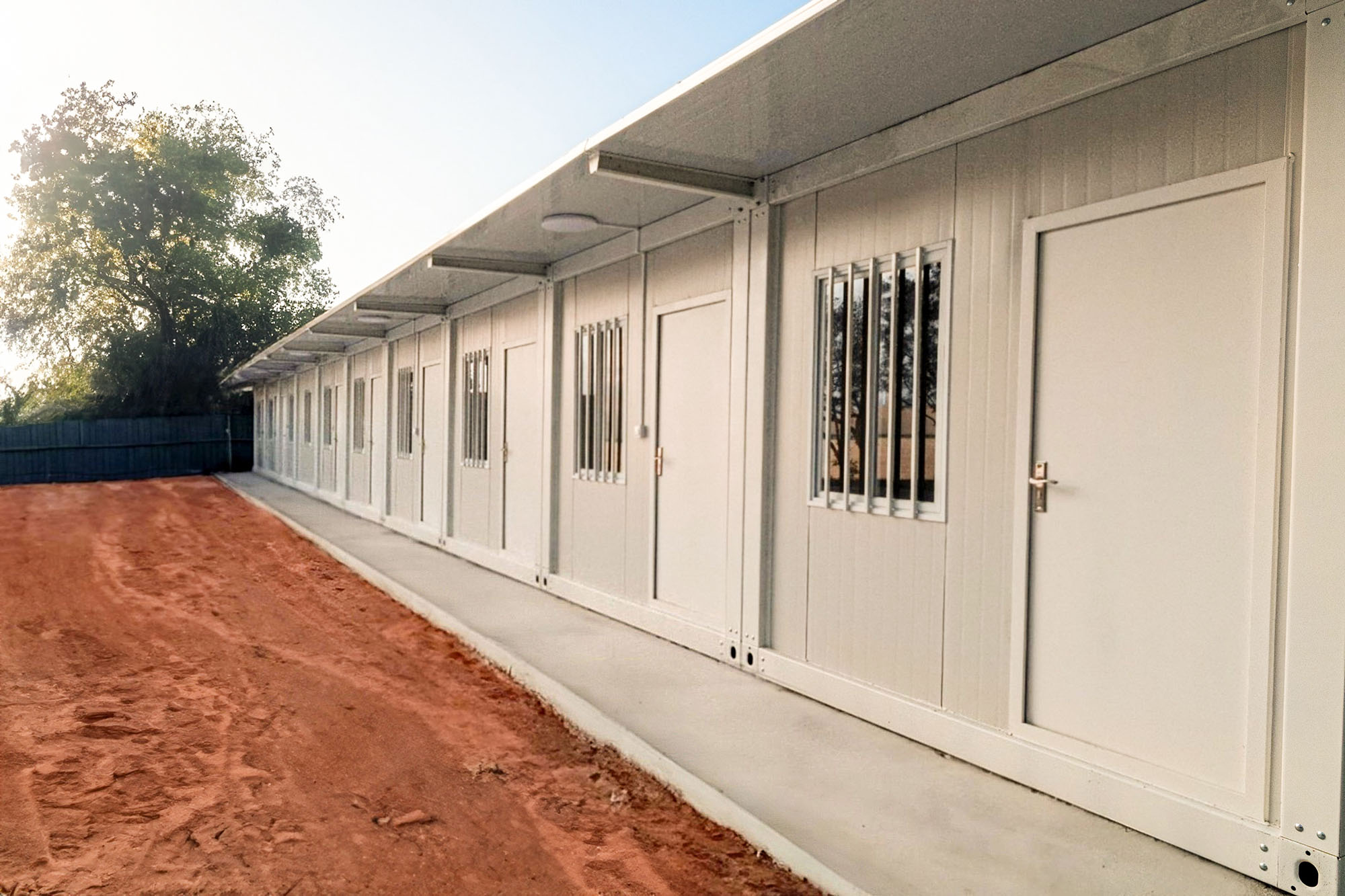 Side view of a sidewalk lining closed doors that open to rooms of worker accommodations.
